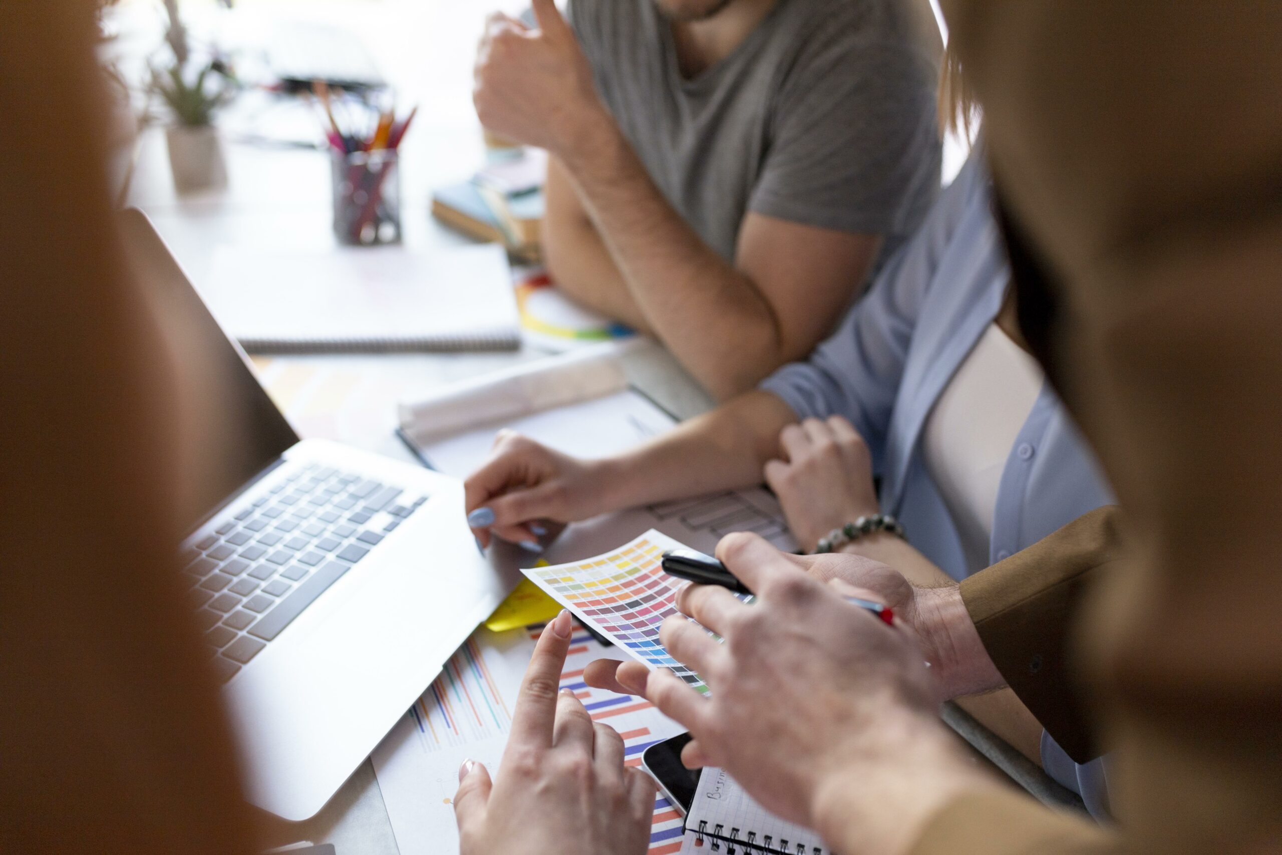 Des personnes en pleine séance de brainstorming autour d'une réunion de travail. Ils échangent des idées et des propositions, concentrés autour d'une table, avec des documents, des ordinateurs portables et des notes éparpillées. L'ambiance est collaborative, chacun partage ses réflexions pour faire avancer le projet commun.